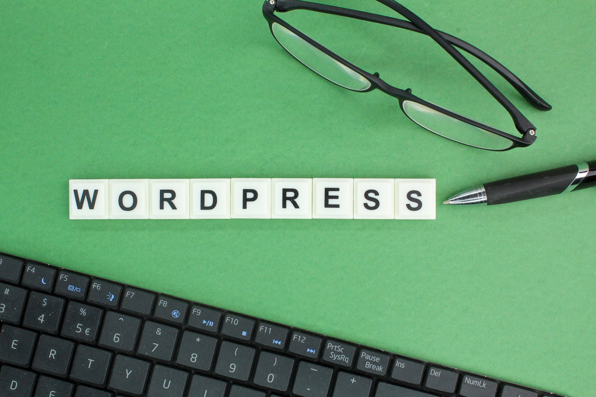 WordPress site kurulumu konusunda bilgilendirici görsel, klavyenin üzerinde 'WORDPRESS' yazan blok harfler ve bir çift gözlük