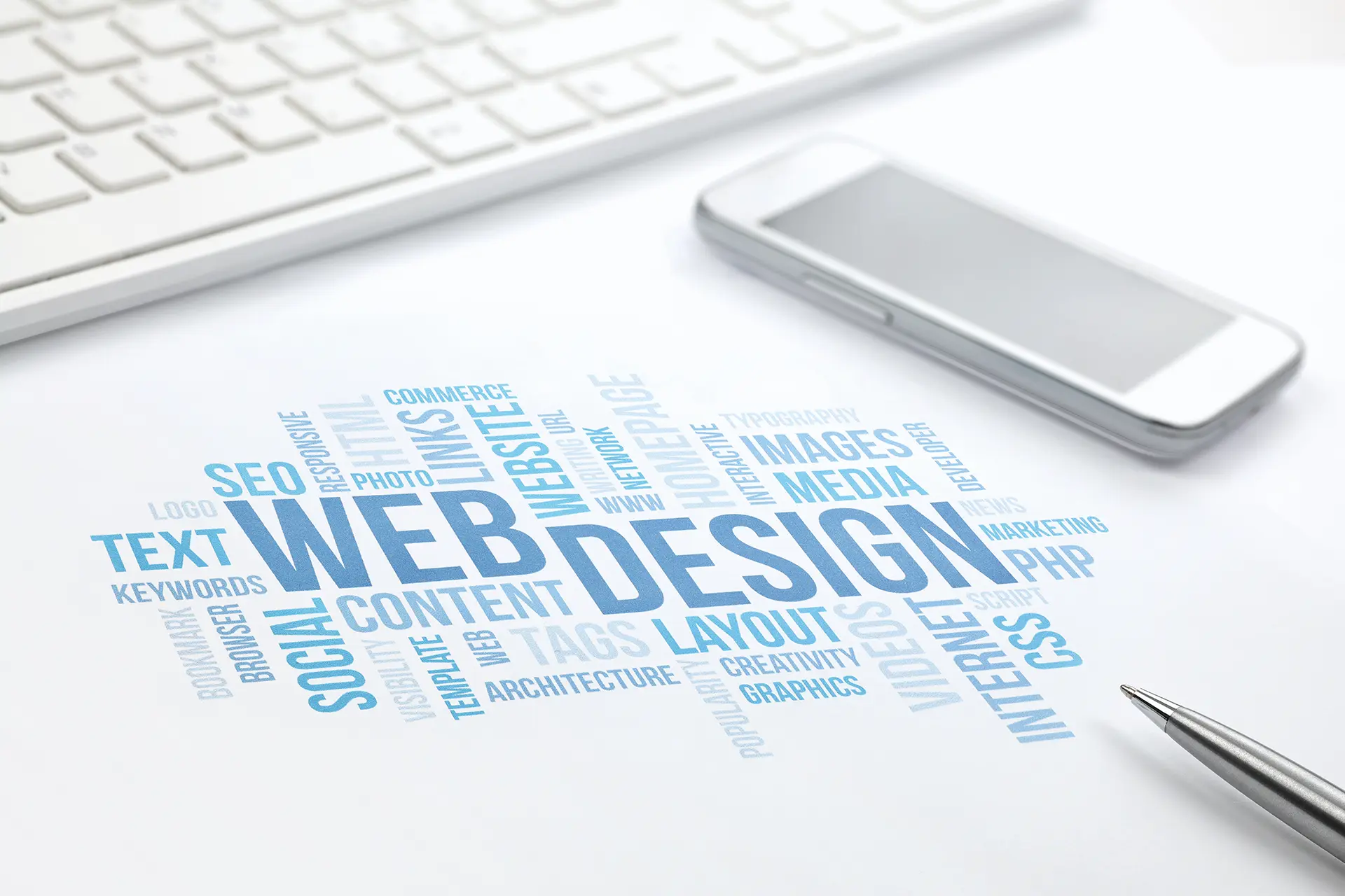 Web tasarım kavramını içeren kelime bulutu ve beyaz bir masa üzerinde klavye ve telefon